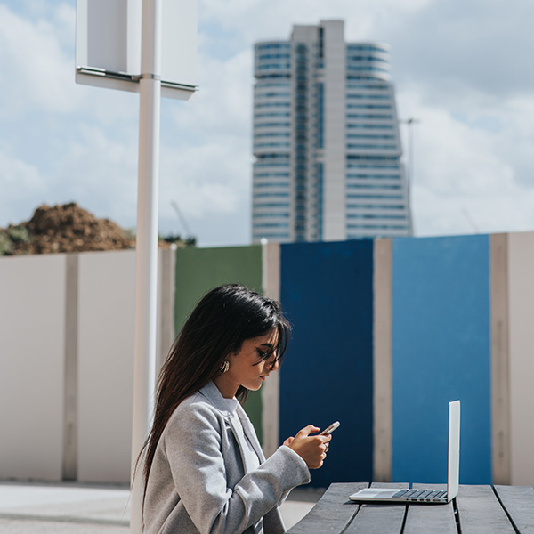 asp woman using her phone and laptop outdoors